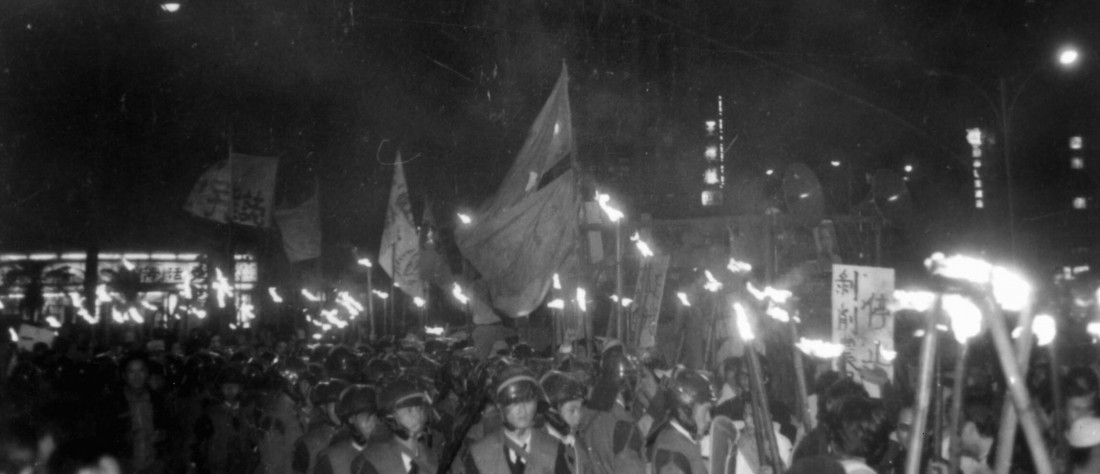 Nighttime protest with a dense crowd, many holding torches and banners in a city street.