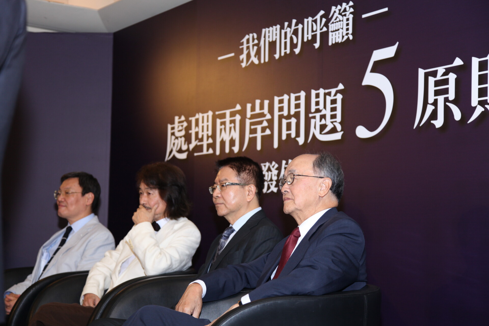 Panel of five men in suits seated in a row on stage, against a purple backdrop with large white Chinese characters behind them.