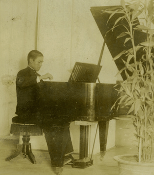 Man in formal attire seated at a grand piano in a sepia-toned vintage photo.