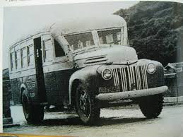 Black-and-white photo of a vintage 1940s bus with a rounded front, parked on a road with trees in the background.