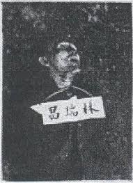 Black-and-white portrait of a man with a tag bearing illegible characters hanging from his neck.