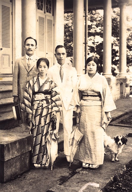Four people in vintage attire pose on a columned veranda; two women in kimonos, two men in suits, with a small dog at the right.