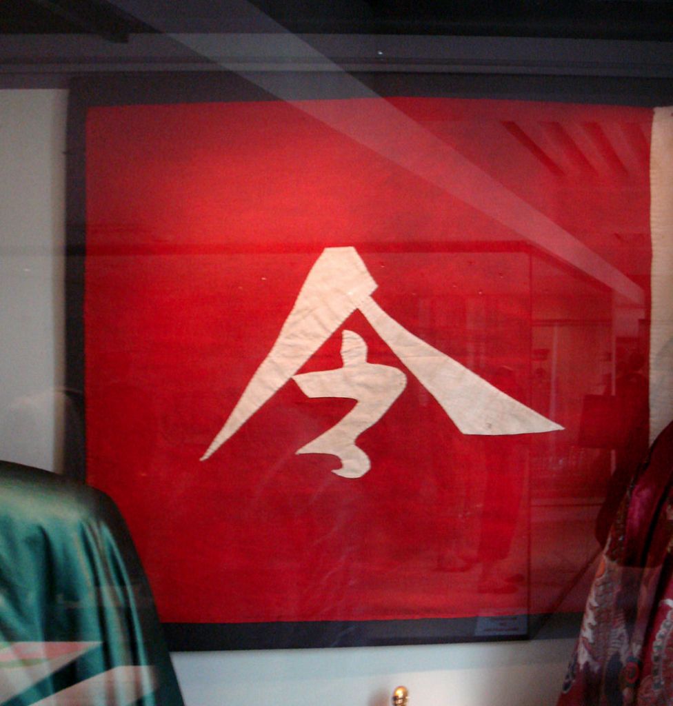 Red poster with a white abstract mountain/triangle logo on a red background, seen through glass.