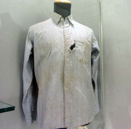 Light gray striped button-down shirt on a mannequin with a torn chest pocket and stains near the chest area.