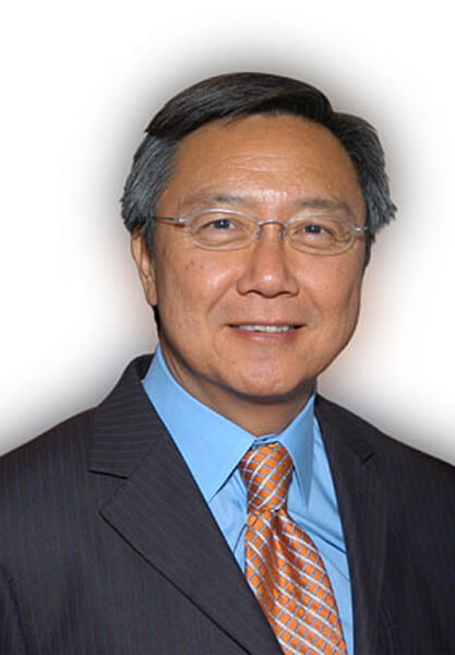 Portrait of a middle-aged Asian man in a dark pinstripe suit, light blue shirt, and orange patterned tie, smiling.