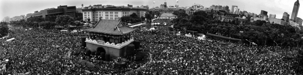 Panoramic view of a large crowd gathered around a traditional Chinese pavilion in a city park.